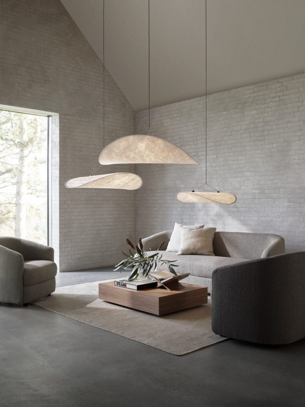 En moderne stue med neutrale toner med minimalistiske møbler. Rummet har et vinklet loft, store unikke pendellamper og et vindue med udsigt over grønne områder.