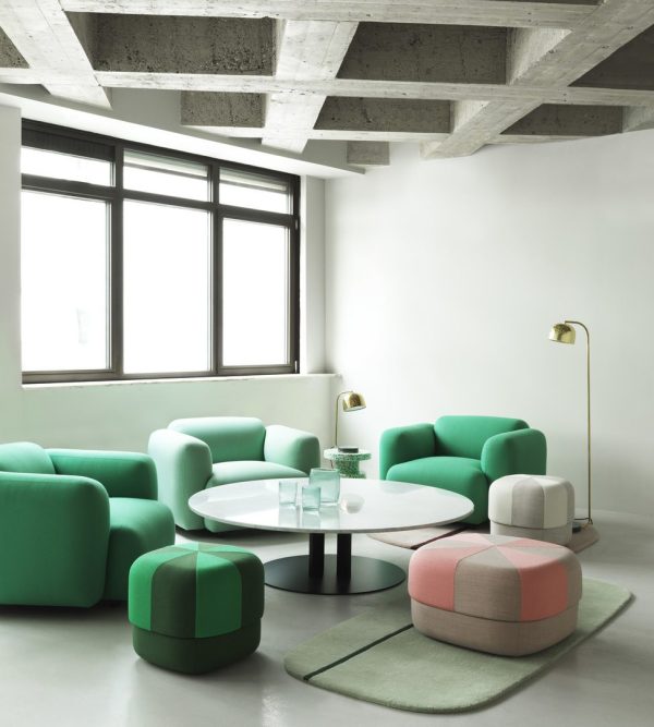 Moderne stue med levende grønne sofaer, NORMANN COPENHAGEN - Circus Puf Duo Stor Ottomans, et hvidt sofabord og en elegant gulvlampe. synligt betonloft og stort vindue, der filtrerer naturligt lys.