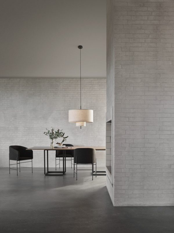 En minimalistisk spisestue med et elegant sort bord med stole, en hængende lampe ovenover og en stor vase med grønt på bordet, omgivet af grå murstensvægge og betongulve. Denne indstilling eksemplificerer principperne for TomorrowsDesign.