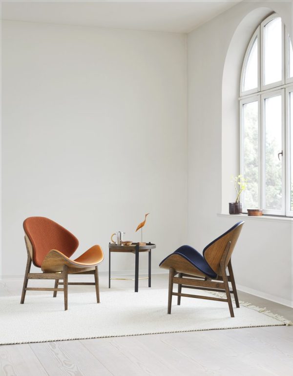 Et minimalistisk værelse med et stort buet vindue, to designerstole vendt væk fra hinanden, en WARM NORDIC - The Orange Loungestol og en blå, ved siden af et lille sort bord med pynteting og en potteplante.