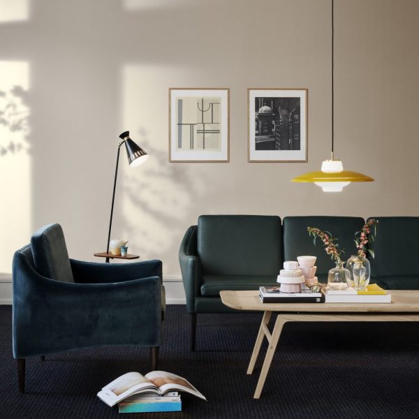 En moderne stue med et mørkegrønt sofasæt med en matchende lænestol, en gulvlampe, pendel, sofabord med bøger og vægkunst. Lyset kaster gennem et vindue og skaber skygger på TomorrowsDesign-væggen.