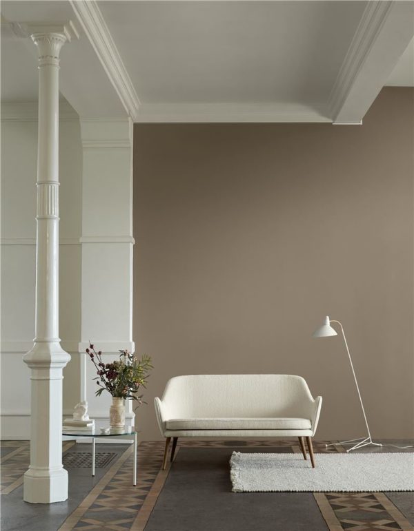 En minimalistisk stue med en WARM NORDIC - Dwell Sofa, en hvid gulvlampe og et lille sofabord. Søjle- og dekorative lister pryder rummet, suppleret med et geometrisk mønstret gulv og en vase med blomster.