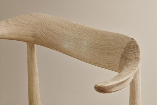 Nærbillede af et træstolsarmlæn, der viser den glatte årring og buede designmøbler mod en blød beige baggrund.