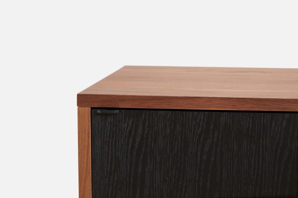 Nærbillede af et moderne design træskab med en kontrasterende mørk tekstureret front og en glat lysebrun top, sat mod en almindelig hvid baggrund.
