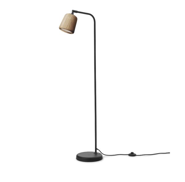 ET NYT VÆRK - Materiale Gulvlampe med et højt, slankt sort stativ og en rund base. Lampen har en vinklet arm, der holder en lille, beige lampeskærm. Strømafbryderen er synligt placeret på ledningen mod en almindelig hvid baggrund.