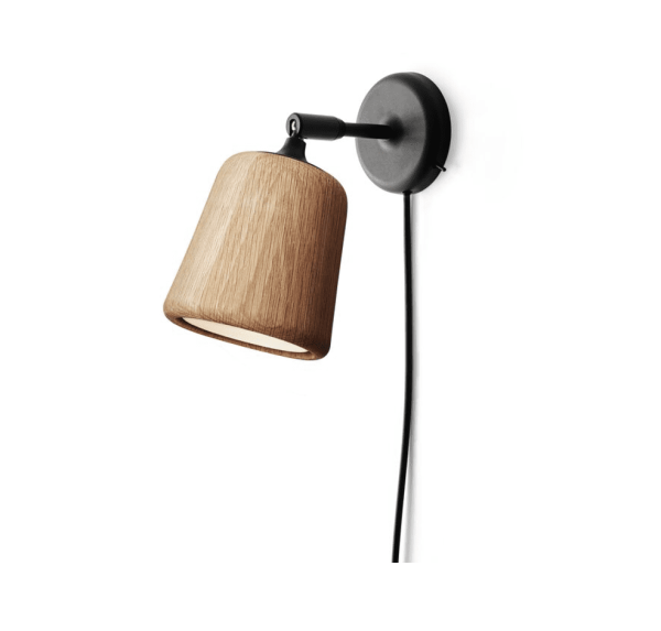 ET NYT VÆRK - Materiale Væglampe med træskærm og sorte metalarmaturer mod en almindelig hvid baggrund. lampens ledning hænger løst under den.