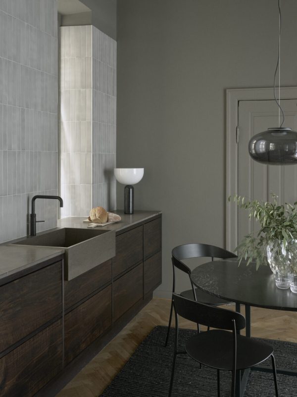 Et moderne køkken med grå vægge, med en træø med integreret vask, et mørkt spisebord med stole fra TomorrowsDesign, store gulvfliser og en dekorativ vase med grønt.