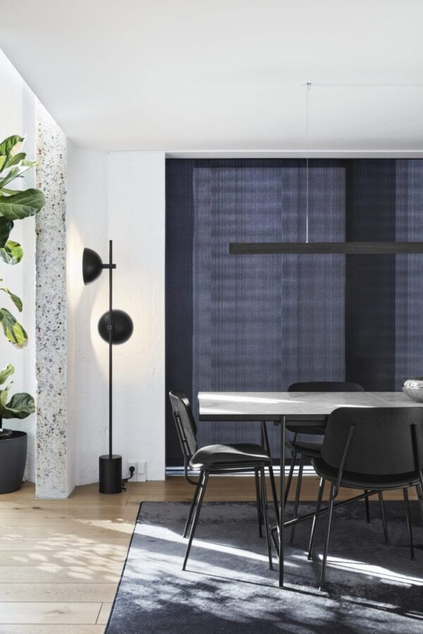 Moderne spiseplads med sort bord, stole og gulvlampe. Mørkeblå gardiner og en hvid terrazzo-søjle supplerer det lyse rum med trægulve og potteplanter. Opsætningen eksemplificerer TomorrowsDesign i alle aspekter af dets interiør.