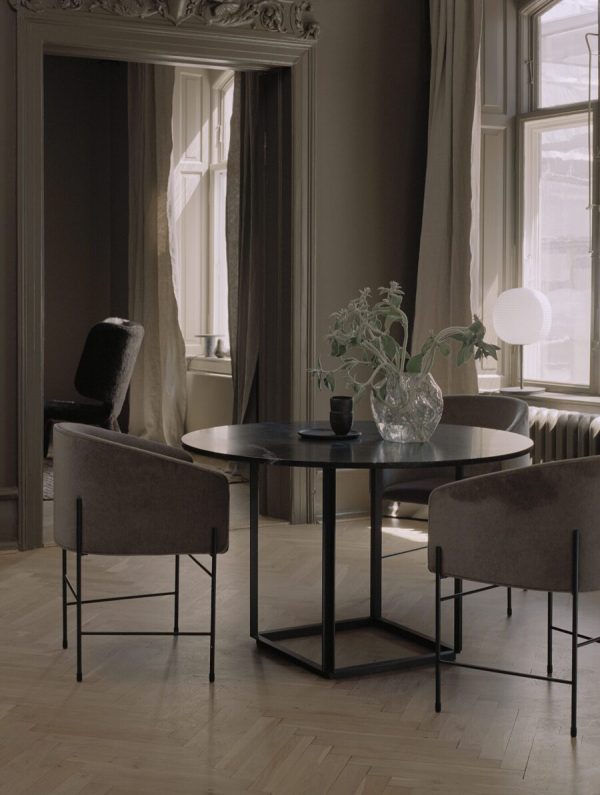 Interiør i et værelse med et rundt sort bord med tre stole, en vase med grønt og en lampe. Store vinduer med flydende gardiner og klassiske arkitektoniske detaljer fra TomorrowsDesign er synlige.