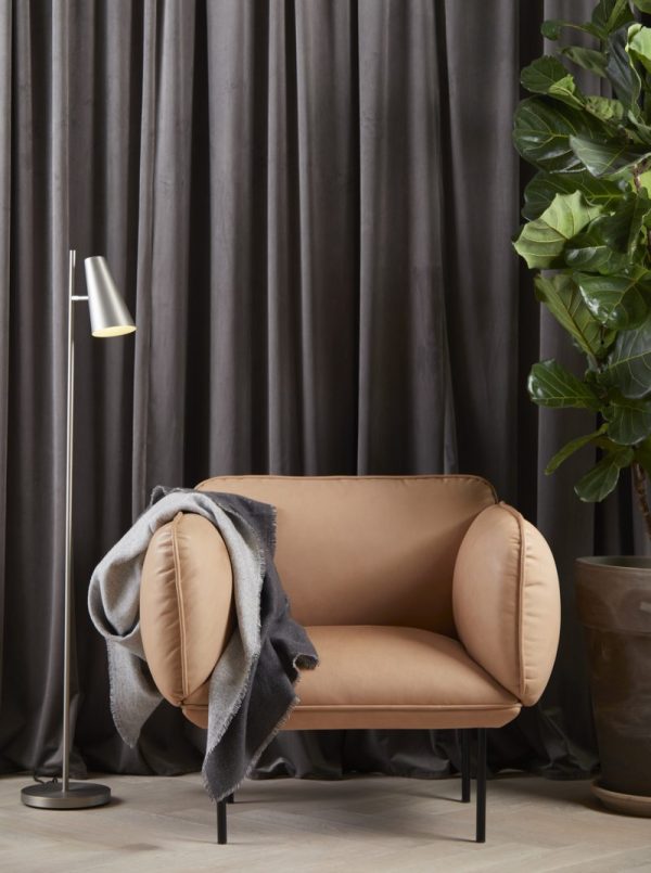 Et hyggeligt læsehjørne med en solbrun polstret lænestol med et gråt tæppe, ved siden af en elegant gulvlampe og en stor potteplante, sat på baggrund af mørkegrå gardiner fra TomorrowsDesign.