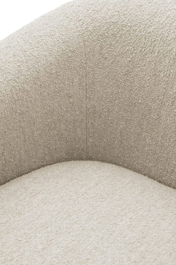 Nærbillede af en beige polstret stol, der viser dens teksturerede stof og buede design. Billedet fokuserer på sømdetaljerne og polstringen af stolen, hvilket fremhæver dens sofistikerede interiørdesign.
