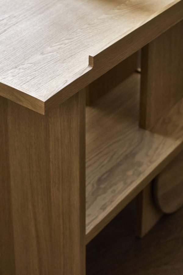 Nærbillede af en KRISTINA DAM - Axis Sidebord, der viser en hakkedetalje på kanten. Bordet har en hylde under, og træets årer ses i den naturlige finish. Billedet fokuserer på Axis Sidebords håndværk og designelementer.