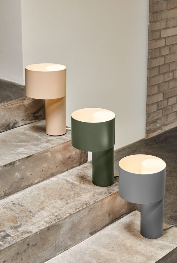 Tre moderne designlamper i beige, grønne og grå farver placeret på betontrin, med en murstensvæg i baggrunden.