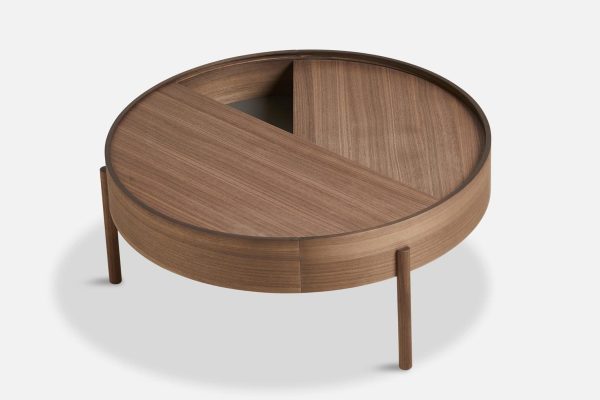 Et rundt sofabord i træ med en yin-yang designplade, der inkluderer en drejelig sektion til opbevaring, stående på tre slanke ben, isoleret på en hvid baggrund. Dette stykke gentager essensen