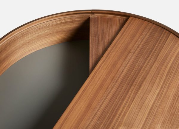 Nærbillede af et moderne designer-rundt træbord med en glat finish, der viser et segment af bordpladen delvist løftet og afslører et skjult rum nedenunder.
