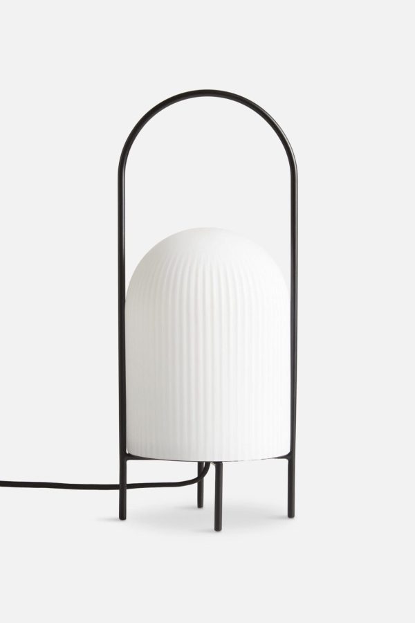 Minimalistisk moderne bordlampe med en rund, ribbet hvid skærm og en tynd, sort, metalbuet ramme fra WOUD - Ghost Bordlampe, på en almindelig hvid baggrund. Lampen er tilsluttet