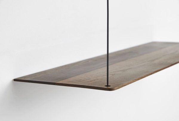 Et nærbillede af en minimalistisk træhylde monteret på en hvid væg, understøttet af en tynd, lodret sort metalstang, afspejler skandinavisk interiørdesign.