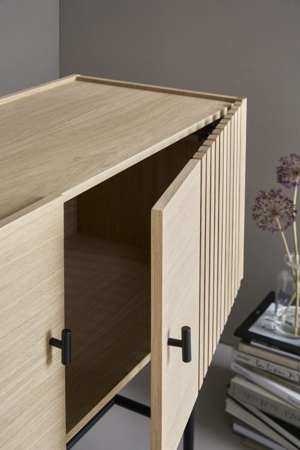 Et nærbillede af en åben, let træskuffe i et skab fra WOUD - Array Skænk, der viser dens slanke design og metalhåndtag. Baggrunden har bløde skygger og en stak bøger.