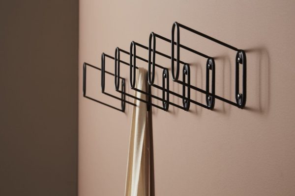 Et minimalistisk sort metalstativ monteret på en beige væg med en enkelt guldfarvet paraply hængende fra en af krogene, legemliggør principperne for Tomorrowsdesign.