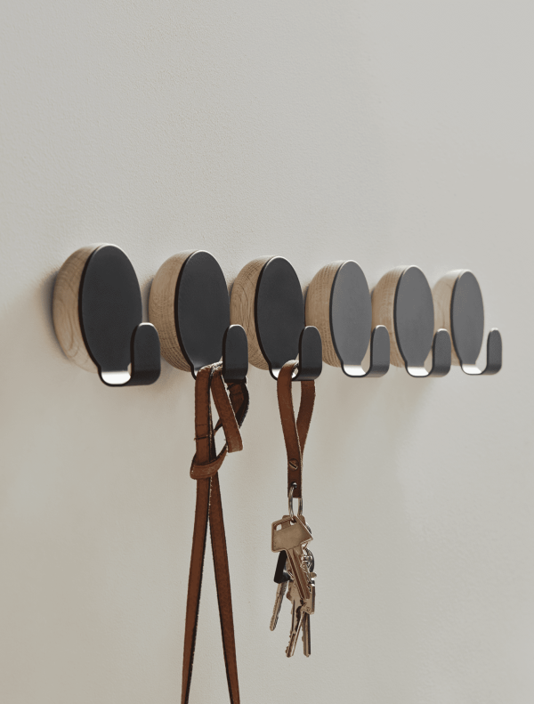 En række vægmonterede trækroge med magnetiske nøgleholdere, hver med en grå metallisk front. To læder nøgleremme med nøgler hænger fra designermøbel krogene til venstre.