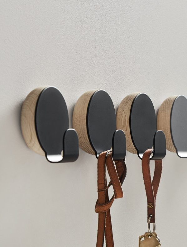 Fire runde vægkroge i træ på en hvid væg, hver med sort front. Tre kroge holder genstande med læderremme med fokus på interiørdesign, og den fjerde krog har et sæt nøgler dinglende