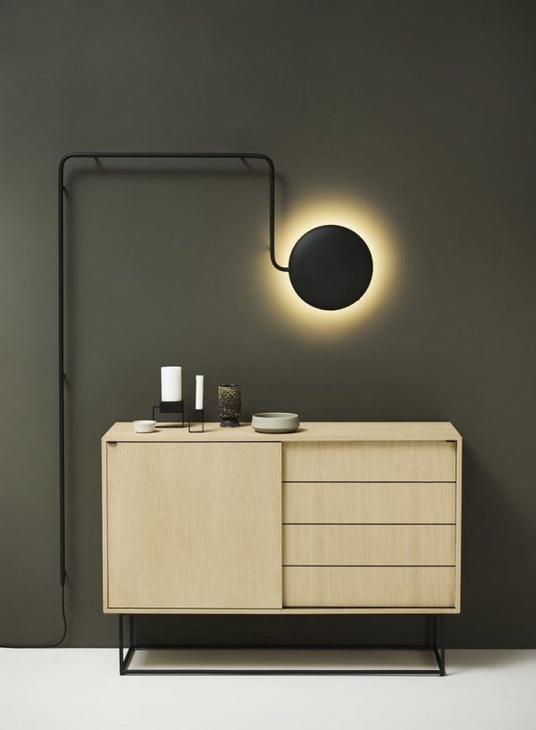 A WOUD - Virka Skænk interiørdesign med et træskab med små, pænt arrangerede pynteting på toppen, under en unik cirkulær lampe monteret på en sort ramme mod en mørkegrå væg.