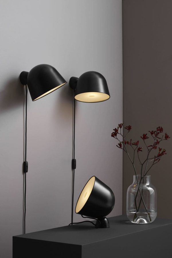 Tre moderne sorte lamper med guldinteriør på mørk hylde, belyst. Ved siden af dem rummer en klar vase rødt løv. Baggrunden er en dæmpet grå, der afspejler banebrydende Tomorrows-design-æstetik