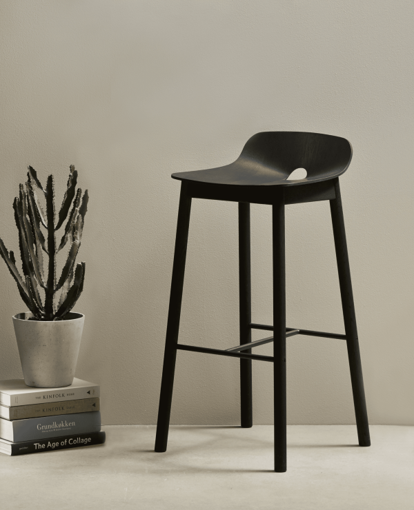 En moderne sort skammel præsenteret på en neutral baggrund, ledsaget af bøger og en dekorativ plante til højre. Sammensætningen antyder en minimalistisk og stilfuld indretning.

Ændret beskrivelse:
En moderne sort skammel præsenteret mod