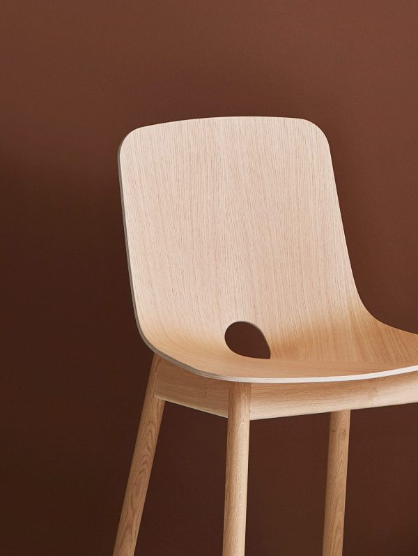 En moderne stol i lyst træ med et enkelt design af Tomorrowsdesign, med buet ryglæn og fire robuste ben, sat mod en almindelig mørkebrun baggrund.