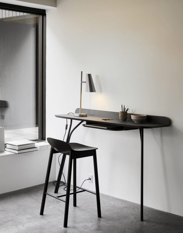 En minimalistisk studieopsætning med et slankt, buet sort skrivebord med matchende skammel, designet af Tomorrowsdesign. Skrivebordet rummer en bærbar computer, notesblok, pen og en skål under et blødt skrivebord