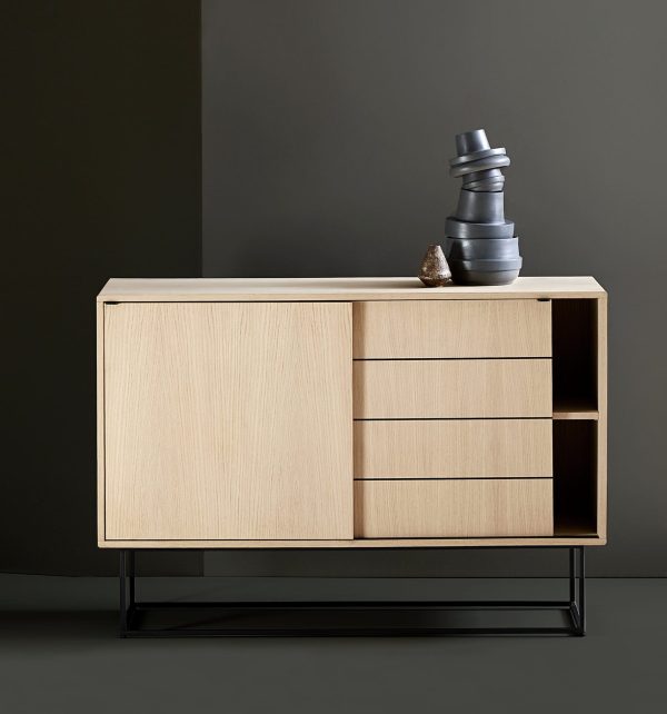 A WOUD - Virka Skænk i beige træfinish med en sort metalramme, med tre skuffer og en åben hylde med en dekorativ sort vase og en lille sten placeret ved siden af, mod en grå baggrund.