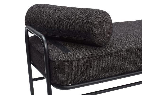 Moderne mørkegrå polstret bænk med en minimalistisk sort metalramme, med en cylindrisk pude, der understøtter den ene ende. Bænken, der repræsenterer Tomorrows design-æstetik, er sat mod en almindelig hvid baggrund