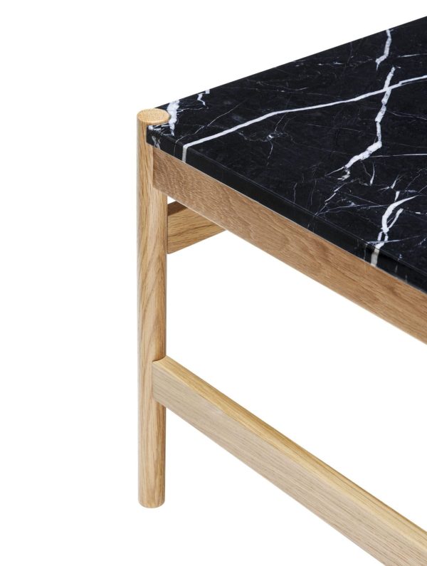 Nærbillede af et moderne sofabordshjørne, designet som et designermøbel, med en sort marmorplade med hvide årer og en lys træramme og -ben, sat mod en hvid baggrund.
