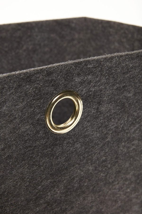Nærbillede af en guldfarvet metaløje på et HÜBSCH - Felt Kurve (sæt af 2) stof. øjet har en glat finish og er centreret i billedet, hvilket giver en kontrast i tekstur og farve mod den matte stofbaggrund.