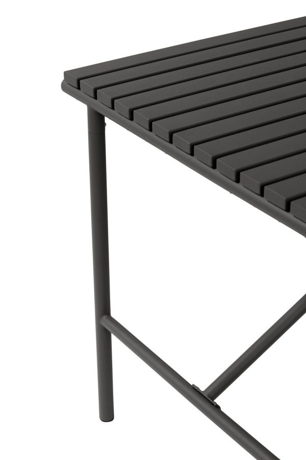 Nærbillede af et sort metalbord med tynde, vandrette lameller på overfladen og et synligt vinklet ben, der viser et slankt, moderne Tomorrows-design.