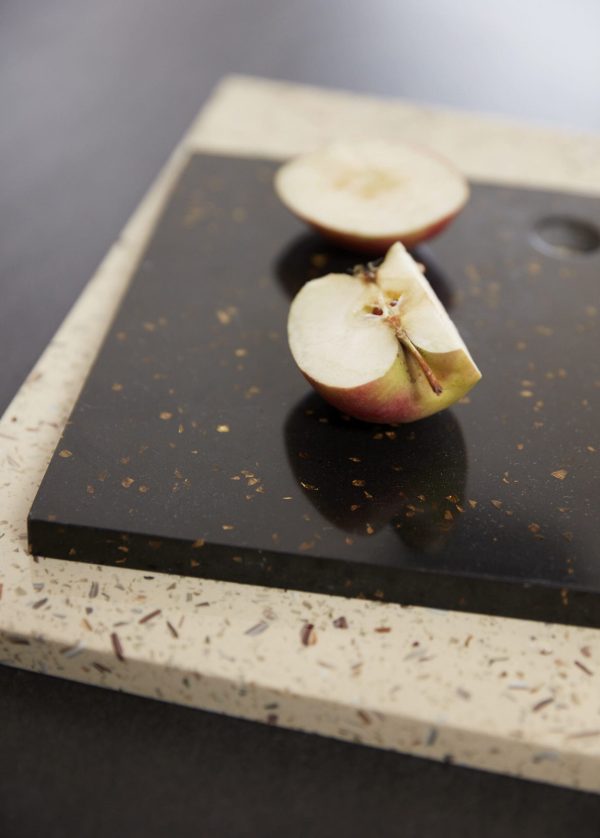 Et æble skåret i halve placeret på et mørkt skærebræt med spættet creme og sort overflade. Æblets indre viser frø og en let brunfarvning, hvilket indikerer eksponering for luft. Skæringen