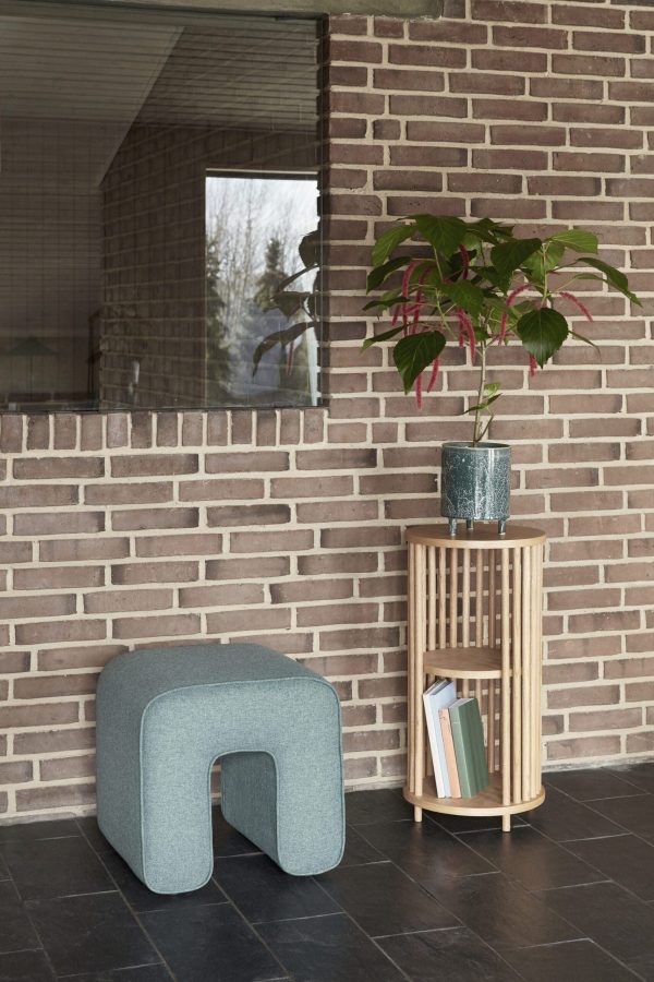 En moderne læsekrog med en HÜBSCH - Sculpture Puf betrukket med turkis og et træsidebord med bøger, toppet med en potteplante. indstillingen er mod en murstensvæg ved siden af et stort vindue.