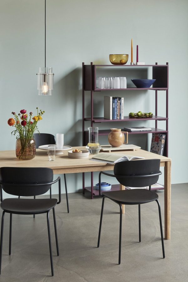 Moderne spisestue med et træbord og sorte stole, en reol fyldt med bøger og indretning og en pendel ovenover. Bordet er dækket med morgenmadsartikler. Rummet indkapsler tom