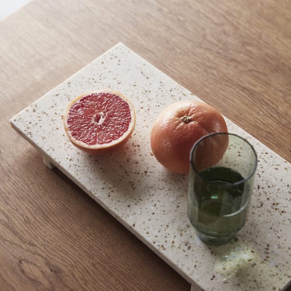En halveret grapefrugt ved siden af en hel grapefrugt på en HÜBSCH - Stone Bakke Terrazzo, med et lille glas grøn juice på et træbord.