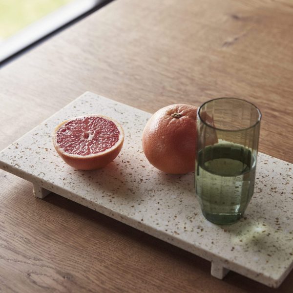 En hel Stone Bakke Terrazzo og en halv ved siden af et grønt glas juice på en spættet bakke, sat på et træbord nær et vindue.