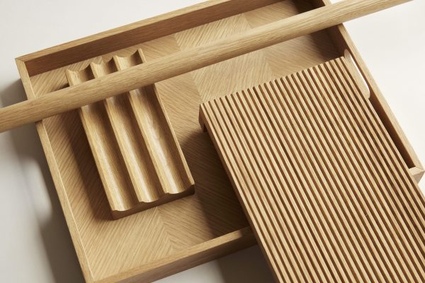Et nærbillede af en minimalistisk træbakke med rum, med en riflet struktur på den ene sektion og en sektion med afrundede slidser til opbevaring af forskellige genstande. Dette stykke viser enestående design i dets struktur og anvendelighed