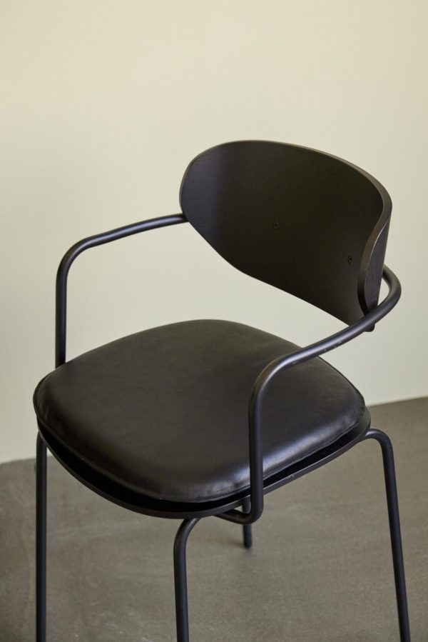 En moderne stol med et sort metalstel og et buet ryglæn, sammen med et rundt, polstret sæde betrukket med sort læder, sat mod en neutral beige baggrund, perfekt til moderne møbler-entusiaster.