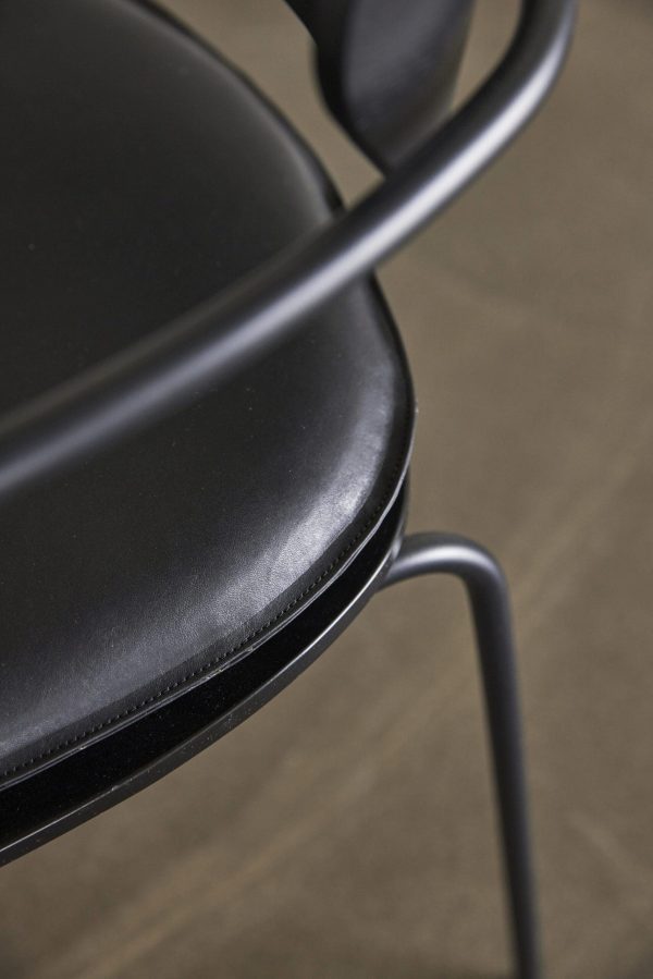 Nærbillede af en HÜBSCH - Arch Spisebordsstol Hynde Sort kontorstol med fokus på armlænet og sædet, der fremhæver dets slanke design og glatte tekstur mod en sløret neutral baggrund.