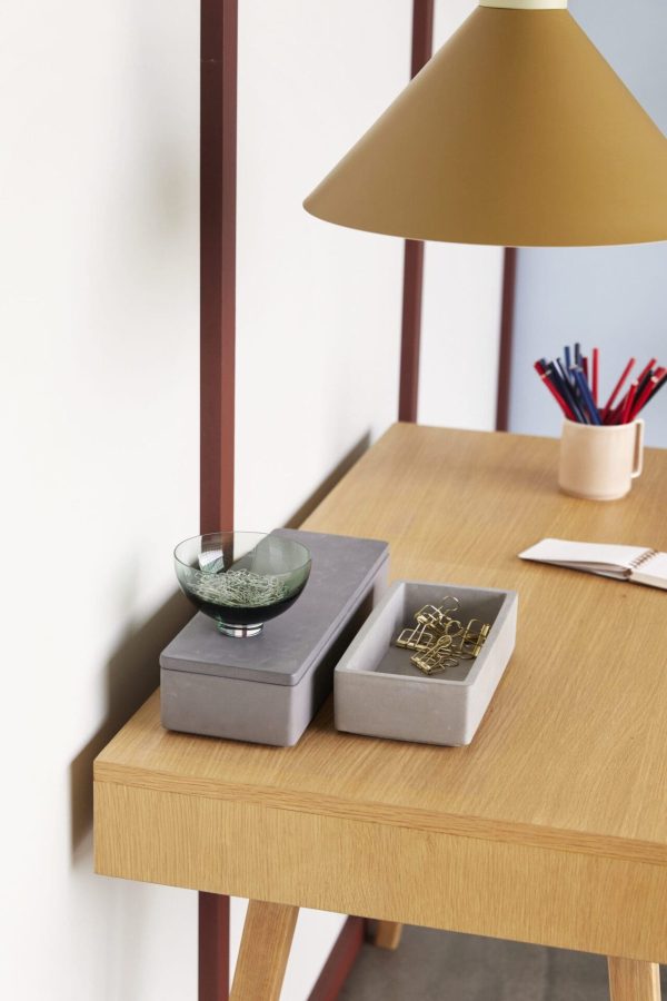 Et velorganiseret skrivebord med to HÜBSCH - Umber opbevaringskasser, den ene med papirclips og den anden en grøn pyntegenstand. en notesbog og kuglepenne er til siden under en stor gul lampe.