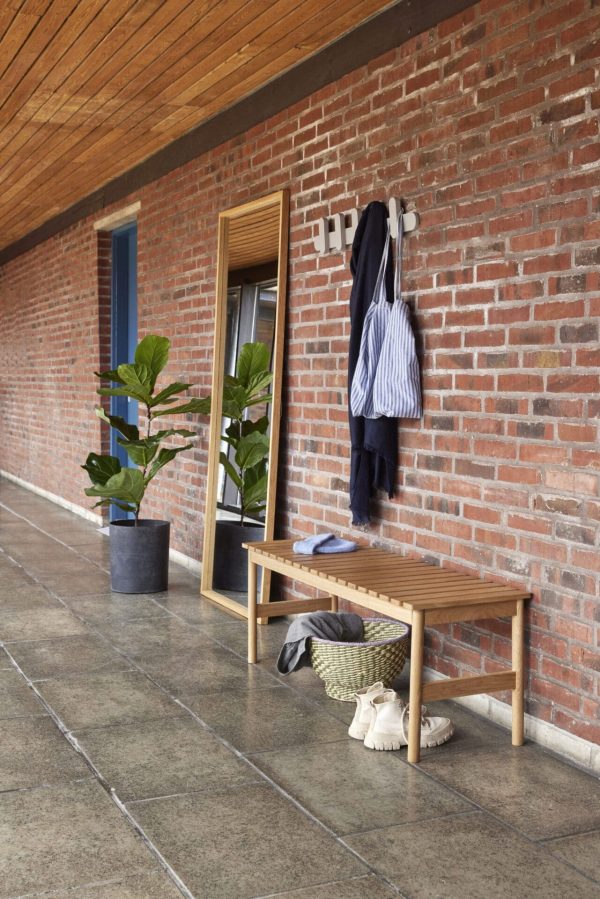 En gang med en murstensvæg med en træbænk med tøj og en taske på designet af Tomorrowsdesign, en plante ved siden af og en dør med blå ramme til venstre