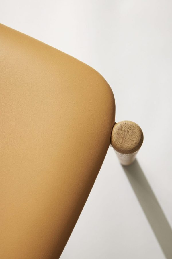 Nærbillede af en minimalistisk designermøbel med en glat solbrun læderoverflade og en afrundet trædetalje, der kaster en skarp skygge på en hvid baggrund.