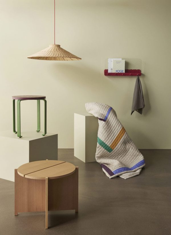 En minimalistisk interiørscene med et tæppe draperet over en moderne stol, en træskammel, stilfulde hylder med håndklæder og en designermøbel pendel. Bløde, neutrale farver dominerer rummet