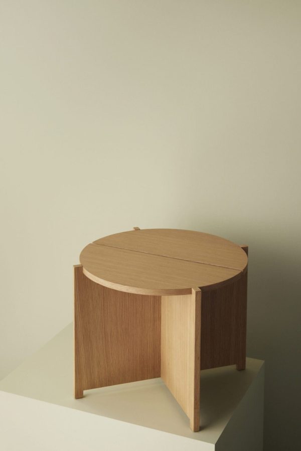Et minimalistisk rundt træbord med lodrette riflede paneler på en lys beige baggrund, der viser en enkel og elegant designermøbel.