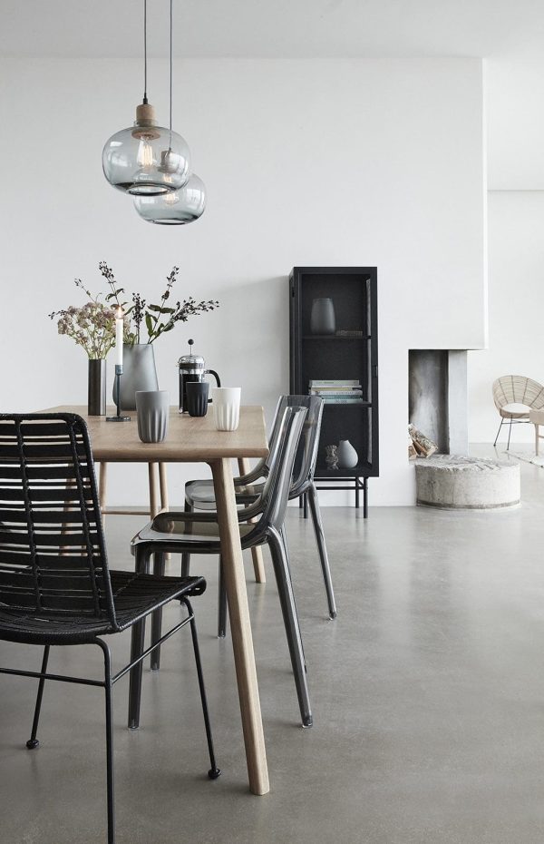 Moderne minimalistisk spiseplads med et træbord, sorte stole, et designer "Tomorrowsdesign" skab og en pejs. Hængende glaslamper og store vinduer skaber et lyst og luftigt rum.