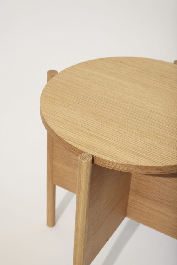 Et nærbillede af en moderne trætaburet med en lys egetræsfinish med et glat, cirkulært sæde og cylindriske ben forbundet med en afrundet Tomorrows-designstøttestruktur.